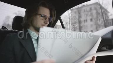 一个英俊的男人，棕色头发，穿着开心果衬衫，灰色西装，戴着眼镜，坐在车里看文件